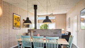Uma sala de jantar com mesa e cadeiras de madeira, uma luminária pendente preta e uma parede de tijolos decorativa.