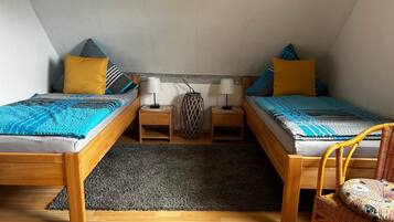 Ein kleines, gemütliches Schlafzimmer mit zwei Holzbetten, einem grauen Teppich und einem Korbstuhl.