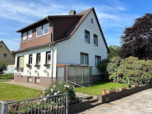 A two-story house with a balcony, a garden with potted plants, and a brick pathway.