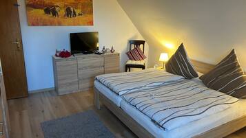 A bedroom with a bed, a TV on a dresser, a painting on the wall, and a nightstand with a lamp.
