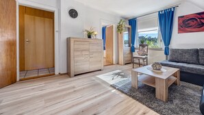 Una sala de estar moderna con piso de madera, un sofá, una mesa de centro y vistas a través de una ventana con cortinas azules.