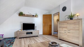 Una sala de estar moderna con un televisor de pantalla plana, muebles de madera, una planta decorativa y un reloj en la pared.