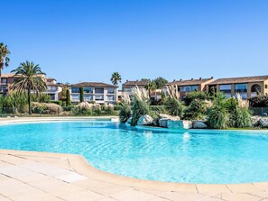 A resort with a swimming pool, palm trees, and Mediterranean-style buildings.