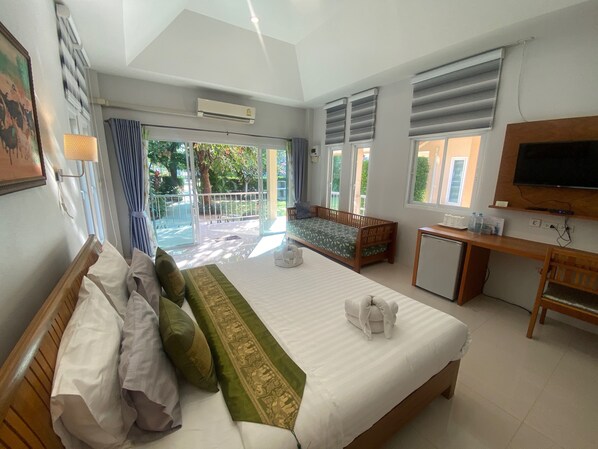 Une chambre d’hôtel avec un grand lit, un bureau, une télévision et un balcon donnant sur un paysage verdoyant.