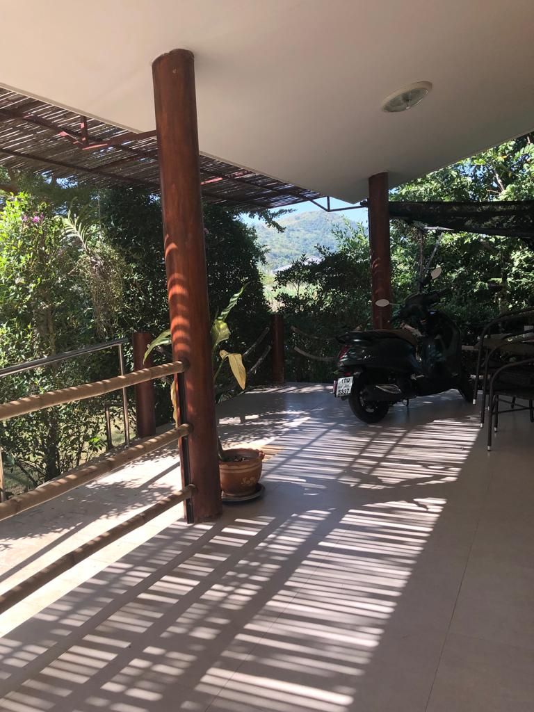 A covered outdoor area with a motorcycle parked, a potted plant, and a railing.