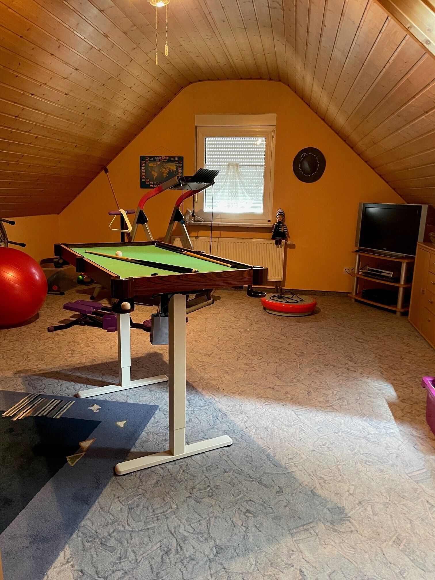 Una habitación con mesa de billar, pelota de ejercicios y televisión.