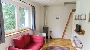 A cozy room with a red sofa, a white chair, a fireplace, a wooden staircase, and a bookshelf.