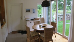 A dining area with a round table, wicker chairs, a ceiling light, and a view of a garden through large windows.