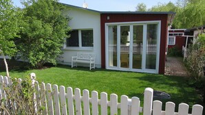 A house with a white fence, a bench, and a red building with glass doors.