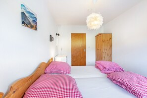 A bedroom with two beds, a wooden wardrobe, a wooden door, and a painting on the wall.