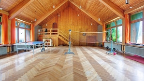 Un salón amplio con techo de madera alto, mesa de ping pong y red de voleibol.