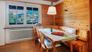 Una habitación con paneles de madera, una mesa, sillas, un banco, una lámpara colgante y un ventanal con vista a follaje.