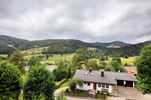 Une maison de campagne avec un toit en tuiles, entourée d’une végétation luxuriante et de collines.