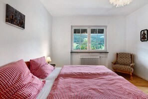 Une chambre à coucher avec un lit, une chaise, une fenêtre donnant sur un beau paysage et un radiateur.