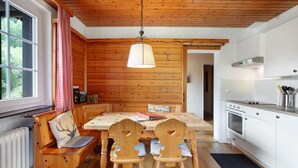 Un interior de madera con una mesa de comedor, sillas, un banco, una lámpara colgante y una zona de cocina.