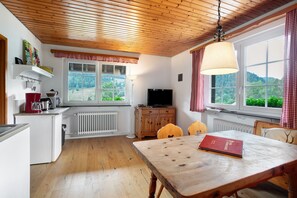 Une cuisine avec un plafond en bois, une table à manger avec des chaises, un téléviseur et une fenêtre donnant sur un paysage verdoyant.