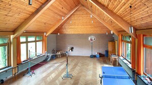 Una habitación amplia con un techo de madera alto, una mesa de ping pong, una mesa de fútbol de mesa y un aro de baloncesto.