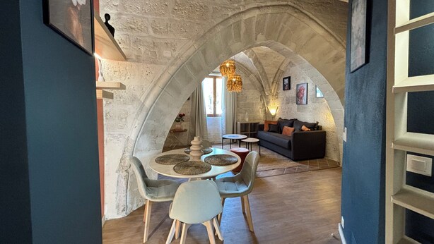 Un interior acogedor con un arco de piedra que da a un comedor con una mesa redonda y sillas, un sofá y una lámpara colgante.