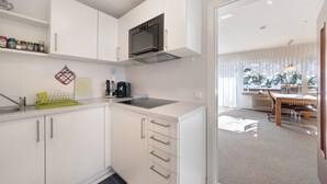 A modern kitchen with white cabinets, a built-in oven, and a dining area with a table and chairs. - 2-room holiday apartment with sun terrace (Schönwald)