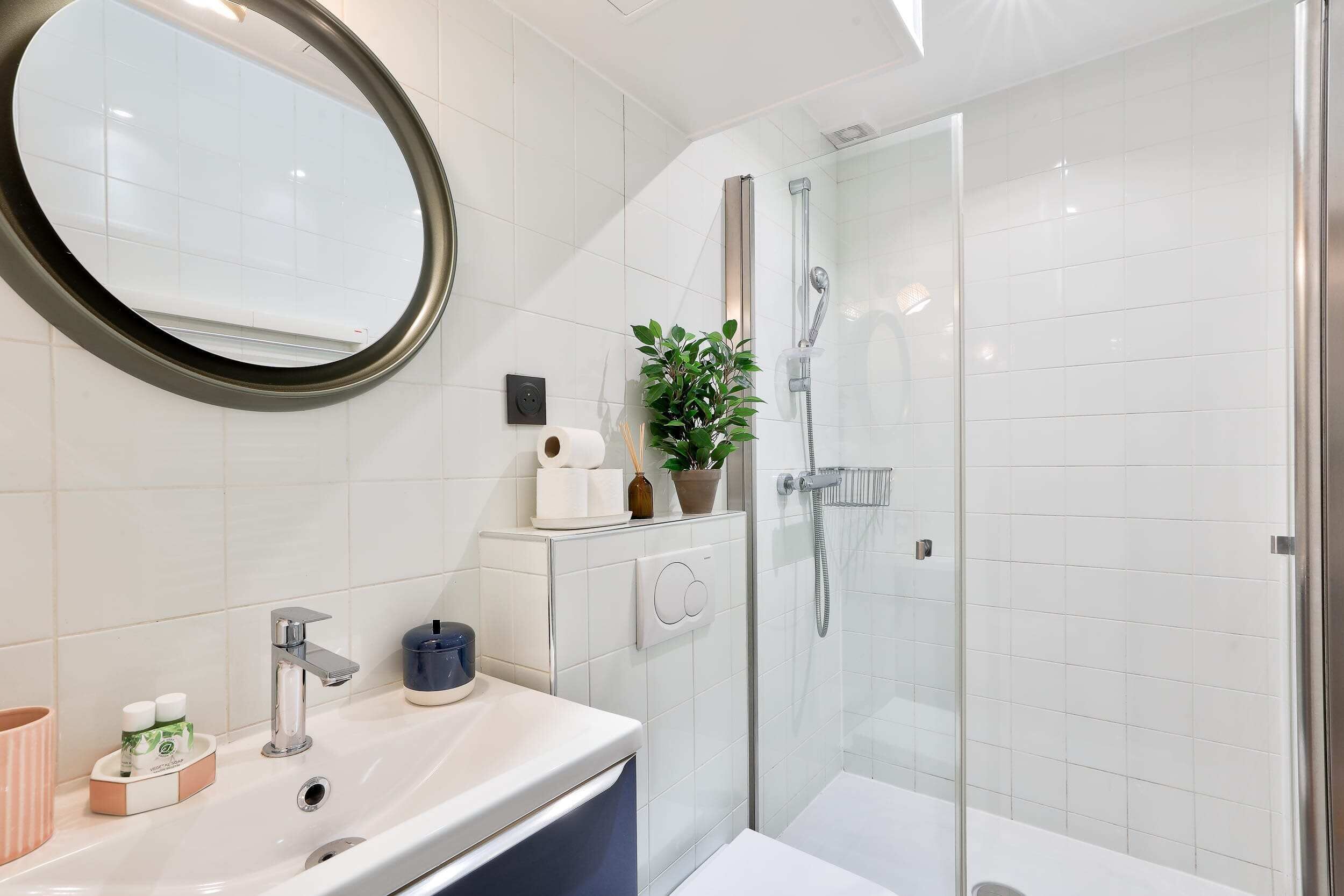 A modern bathroom with a white sink, a mirror, a shower, and a potted plant.