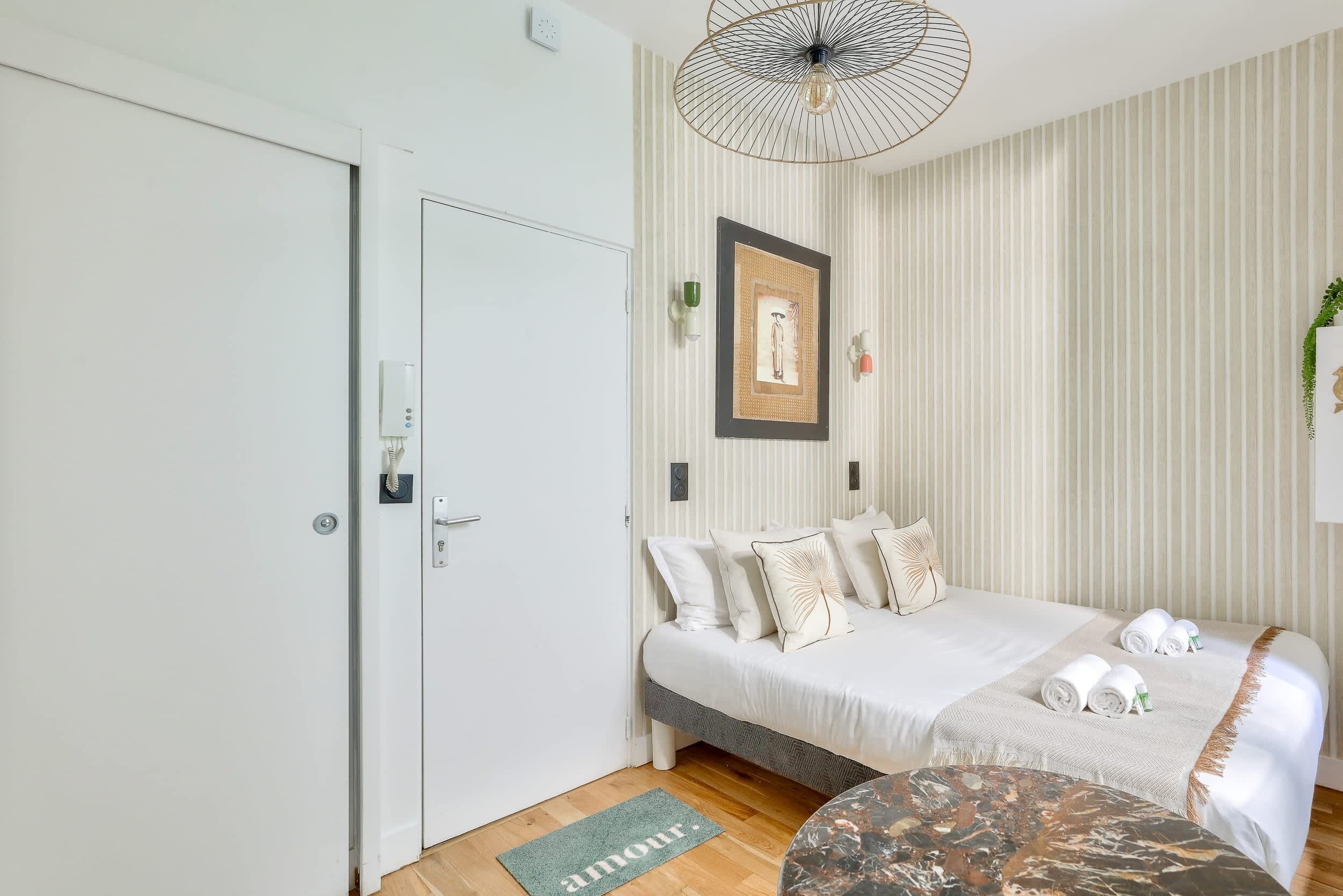 Un dormitorio moderno con cama, mesitas de noche, lámpara colgante y un cuadro enmarcado en la pared.