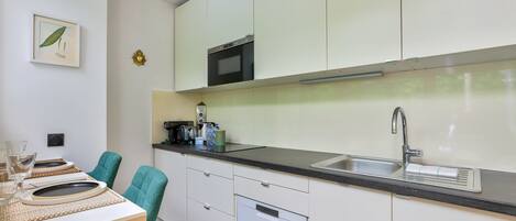 Una cuina moderna amb armaris blancs, un microones negre, un rentaplat i una zona de dinar amb taula i cadira.