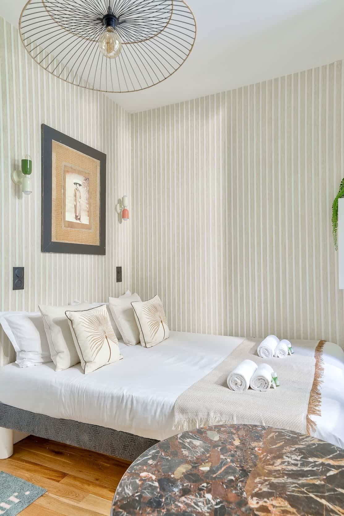 A hotel room with a bed, a round table, and a wall-mounted light fixture.