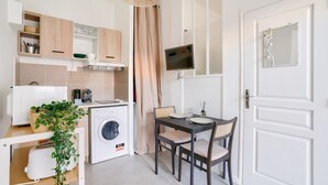 Cocina compacta con lavadora, una mesa de comedor con sillas y un televisor montado en la pared.