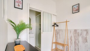 Una habitación con un escritorio de madera oscura, una planta en maceta, un perchero de madera y una puerta que da a otra habitación.