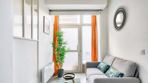Una sala de estar moderna con un sofá gris, una planta en maceta y un espejo redondo en la pared.