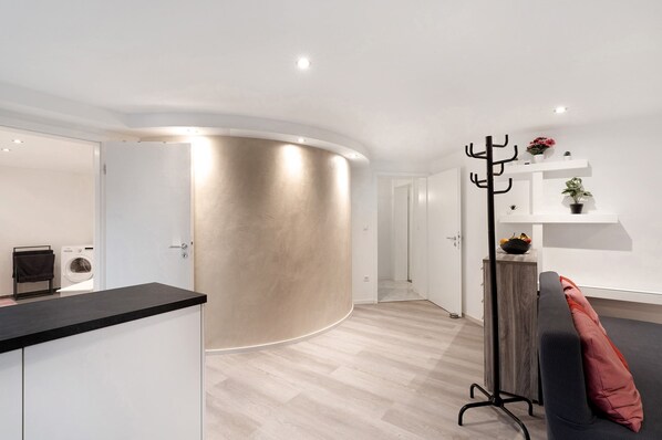 A modern interior with a curved wall, a black countertop, a grey sofa, and a coat rack with plants.