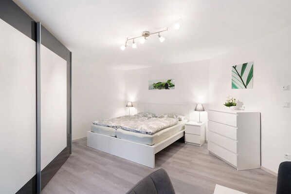 Une chambre à coucher moderne, comprenant un lit, des tables de chevet, une commode et un luminaire fixé au plafond.