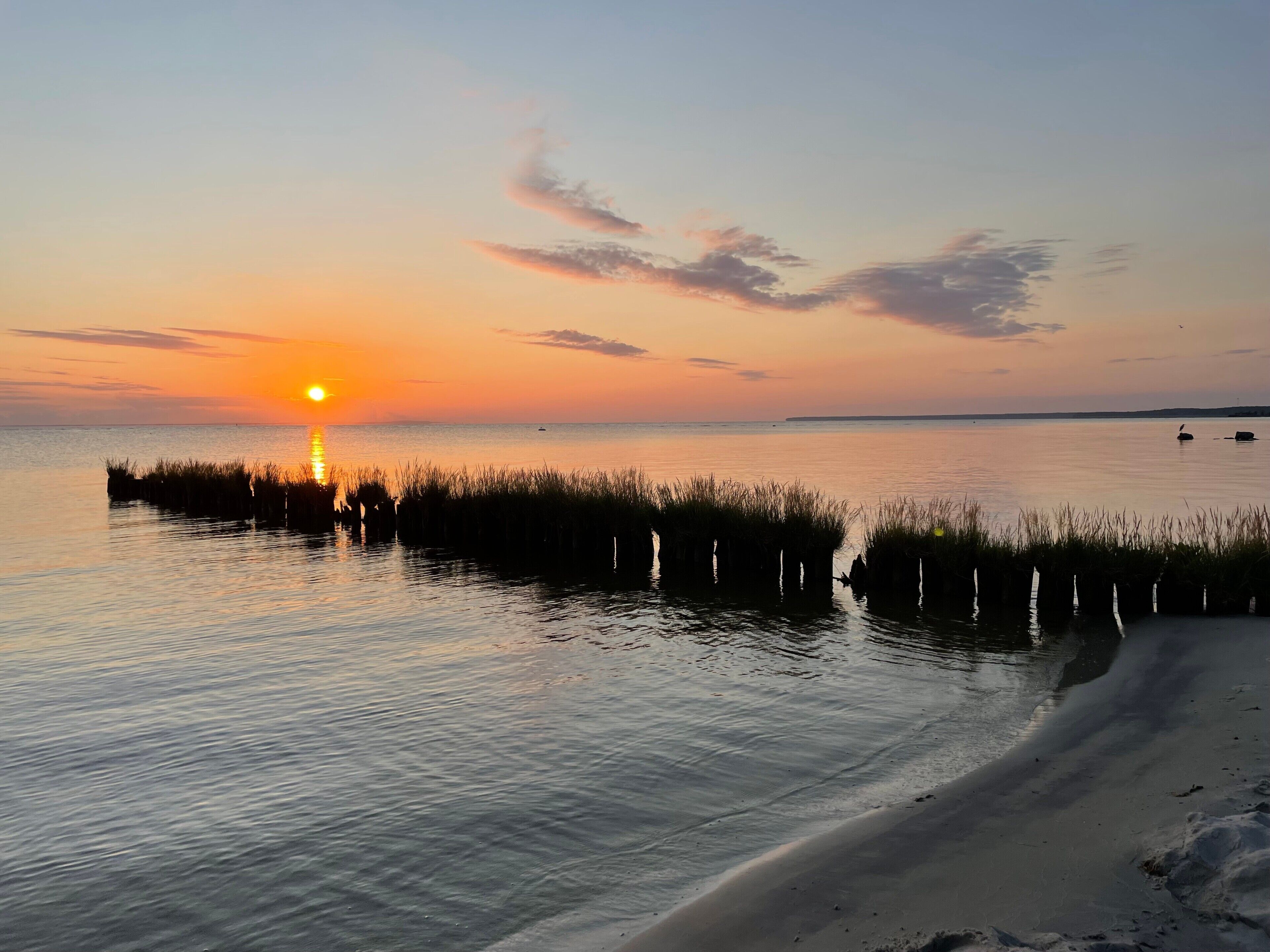 Un coucher de soleil sur une étendue d'eau calme, avec une plage de sable au premier plan.