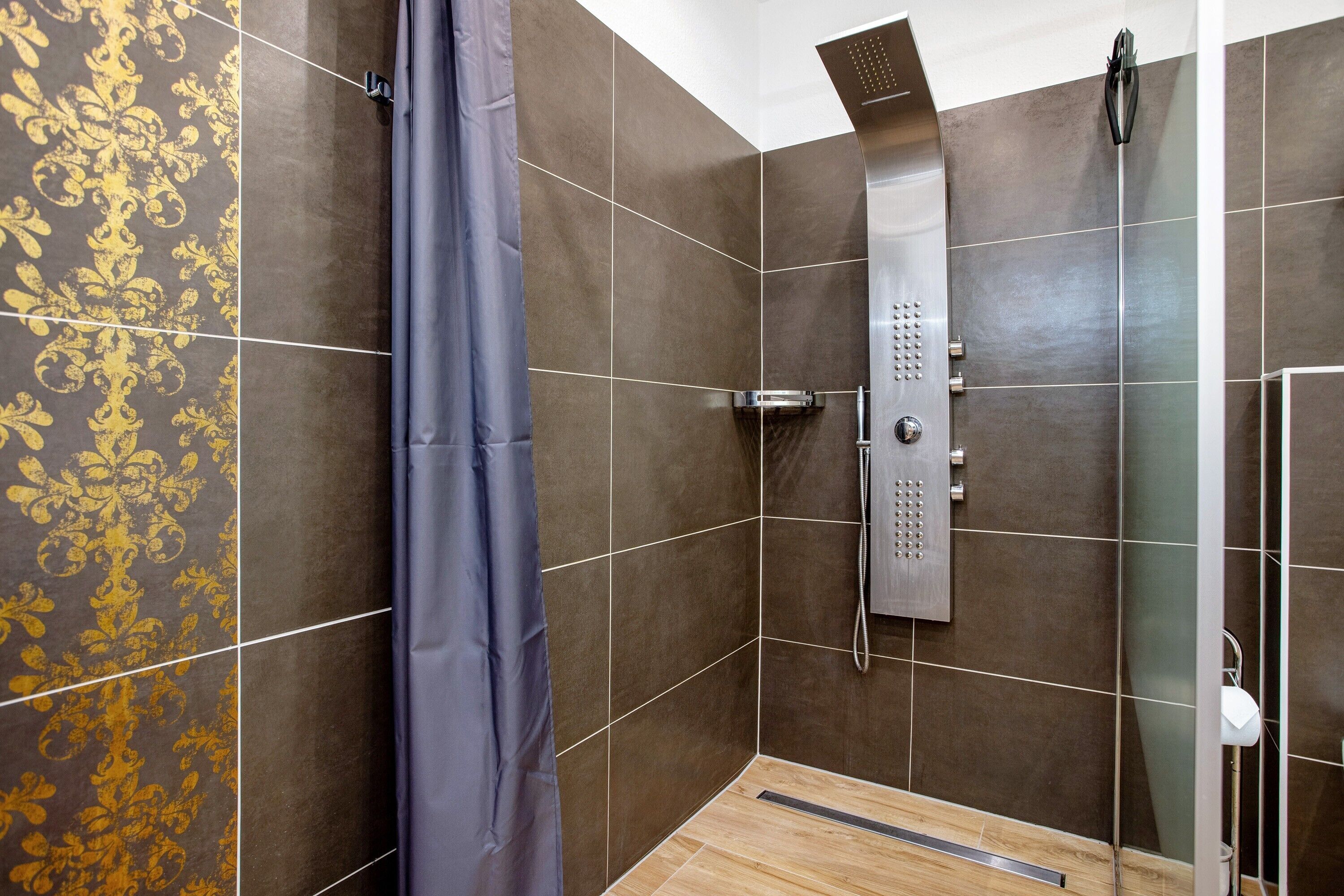 A shower area with a showerhead, a curtain, and a tiled wall.