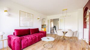 Un salon moderne avec un canapé rouge, une table basse blanche et un coin repas comprenant une table ronde et des chaises.