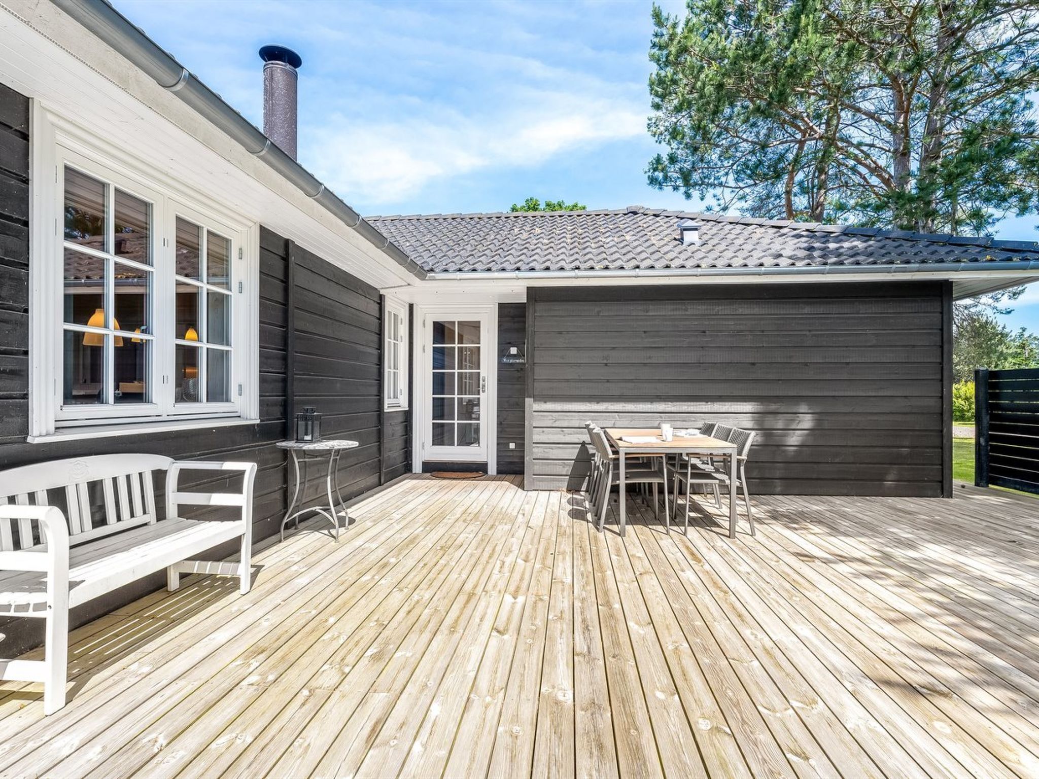A wooden deck with a table and chairs, a bench, and a garage door.