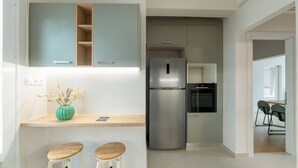 A modern kitchen with a stainless steel refrigerator, a built-in oven, and a wooden countertop. There are two wooden stools and a green vase with dried plants. - Charismatic 2BR Apartment in Hilton (Athina)