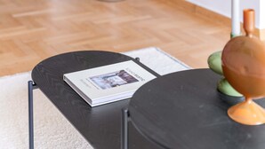 A modern living room with a wooden floor, a black round table with a magazine, a potted plant, and a candle holder. - Charismatic 2BR Apartment in Hilton (Athina)