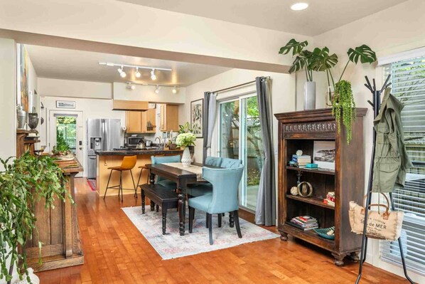 A modern kitchen with wooden cabinets, a dining area with a table and chairs, and a bookshelf with various items. - Spacious SW Portland 4BR/3BA | 2 King Suites | 15min to Downtown | Groups of 8 (Portland)