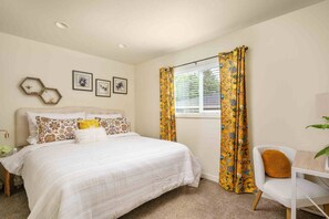 A bedroom with a bed, a chair, a window with curtains, and wall art. - Spacious SW Portland 4BR/3BA | 2 King Suites | 15min to Downtown | Groups of 8 (Portland)