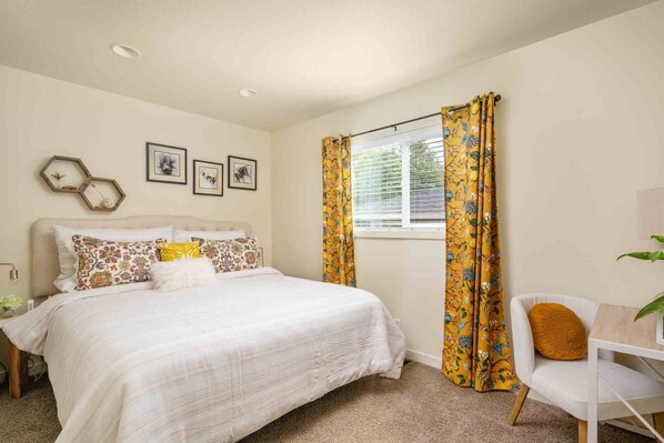 A bedroom with a bed, a chair, a window with curtains, and wall art.