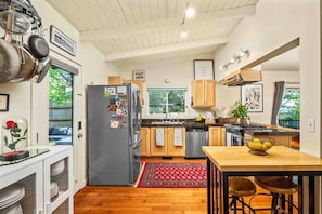 A modern kitchen with wooden cabinets, a stainless steel refrigerator, a stove, and a dining area with stools.