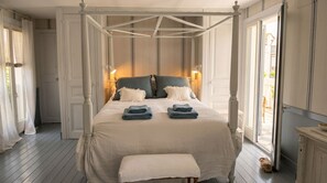 Un lit à baldaquin avec des poteaux aux quatre coins, un banc au pied du lit et deux lampes de chevet.