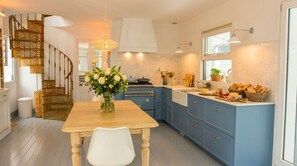 Une cuisine moderne avec des meubles de rangement bleus, une table à manger en bois et un escalier en colimaçon.