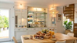 Een keuken met een houten tafel gedekt voor het ontbijt, een glazen vitrinekast en een hangende lamp.