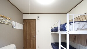 A dormitory room with bunk beds, a wooden door, a coat rack with hangers, and a bulletin board with papers. - 203_Shinjuku Gourmet&Shopping Recently (新宿区)