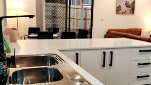 Eine moderne Küche mit Edelstahlgeräten, ein Essbereich mit Stühlen und ein braunes Sofa.