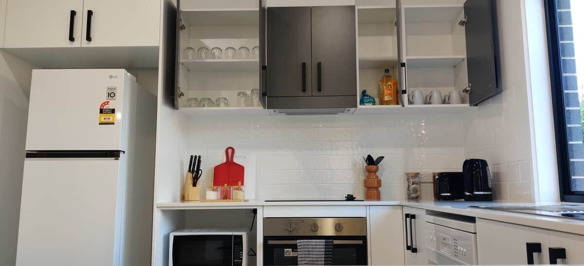 Een moderne keuken met witte kastjes, een roestvrijstalen koelkast, een koffiezetapparaat en een magnetron.