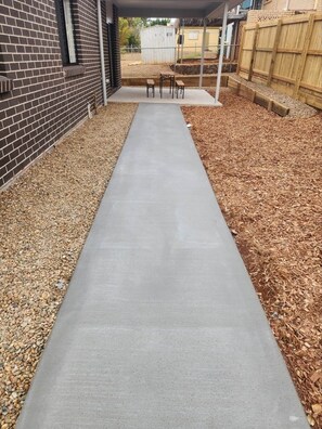 Un sendero de concreto que lleva a un patio cubierto con una mesa y sillas.
