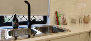 A kitchen with a stainless steel sink, a bottle of dish soap, and a cookbook on the counter.
